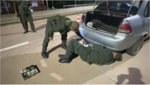Gendarmes revisan el paragolpes trasero de un auto junto a paquetes de cigarrillos incautados.