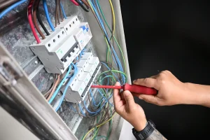Una persona trabaja con un destornillador en un tablero eléctrico con cables y protecciones.