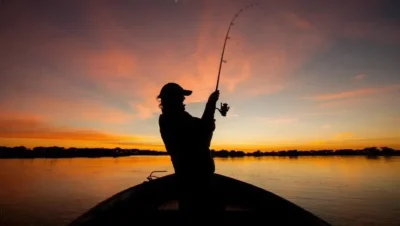 Silueta de una persona con caña de pescar sobre una embarcación al atardecer.